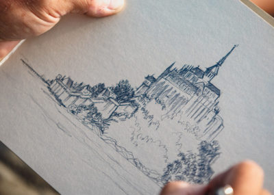 Artiste dessinant le Mont-Saint-Michel au crayon, focus sur ses mains et son dessin