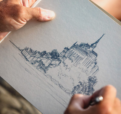 Artiste dessinant le Mont-Saint-Michel au crayon, focus sur ses mains et son dessin