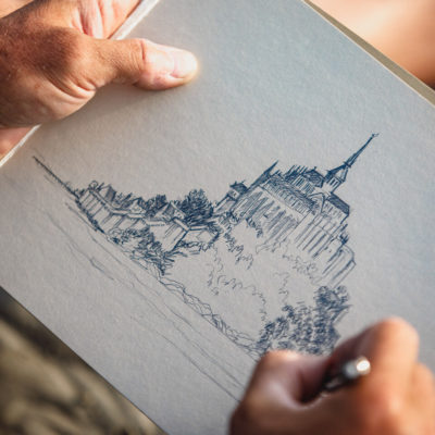 Artiste dessinant le Mont-Saint-Michel au crayon, focus sur ses mains et son dessin