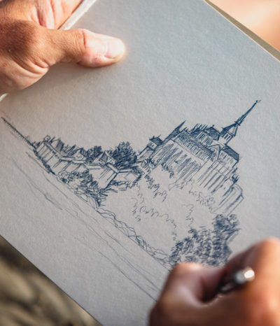 Artiste dessinant le Mont-Saint-Michel au crayon, focus sur ses mains et son dessin