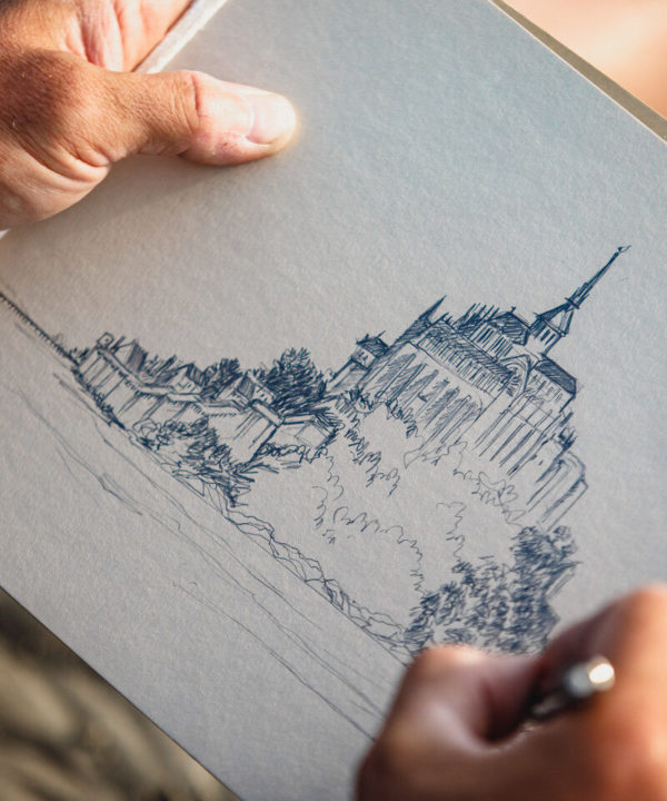 Artiste dessinant le Mont-Saint-Michel au crayon, focus sur ses mains et son dessin
