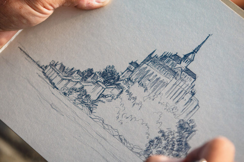 Artiste dessinant le Mont-Saint-Michel au crayon, focus sur ses mains et son dessin