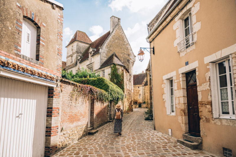 Rue grimpante pavée de Mortagne-au-Perche. Le soleil est présent. Une personne y marche.
