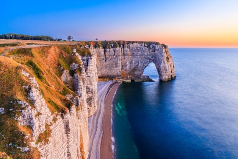 Falaises blanches d’Étretat en Normandie illuminées par les couleurs chaudes du coucher de soleil, face à la mer.