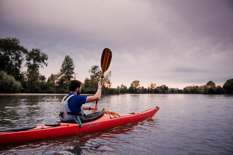 Homme de dos réalisant du canoë-kayak au coucher du soleil