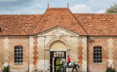 Bâtiment du Haras National du Pin avec cavalier entraînant son cheval devant