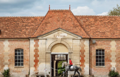 Bâtiment du Haras National du Pin avec cavalier entraînant son cheval devant