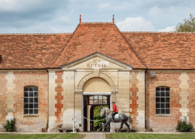 Bâtiment du Haras National du Pin avec cavalier entraînant son cheval devant
