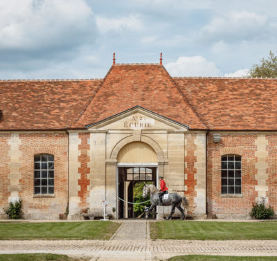 Bâtiment du Haras National du Pin avec cavalier entraînant son cheval devant