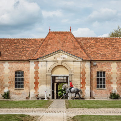 Bâtiment du Haras National du Pin avec cavalier entraînant son cheval devant