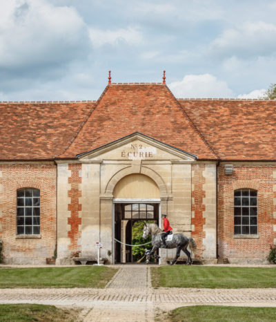 Bâtiment du Haras National du Pin avec cavalier entraînant son cheval devant
