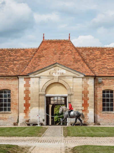 Bâtiment du Haras National du Pin avec cavalier entraînant son cheval devant
