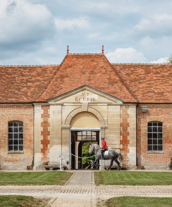 Bâtiment du Haras National du Pin avec cavalier entraînant son cheval devant