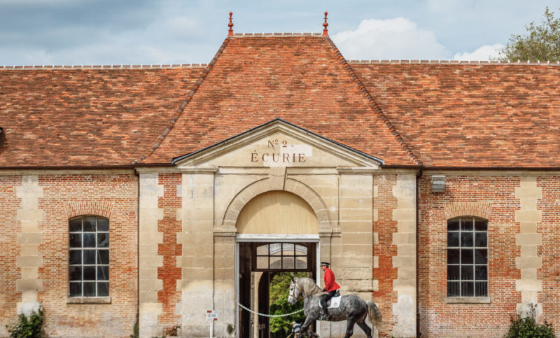 Bâtiment du Haras National du Pin avec cavalier entraînant son cheval devant