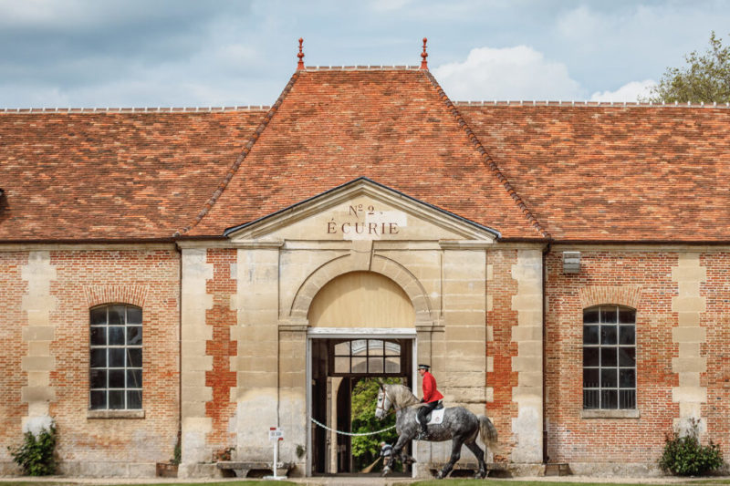 Bâtiment du Haras National du Pin avec cavalier entraînant son cheval devant