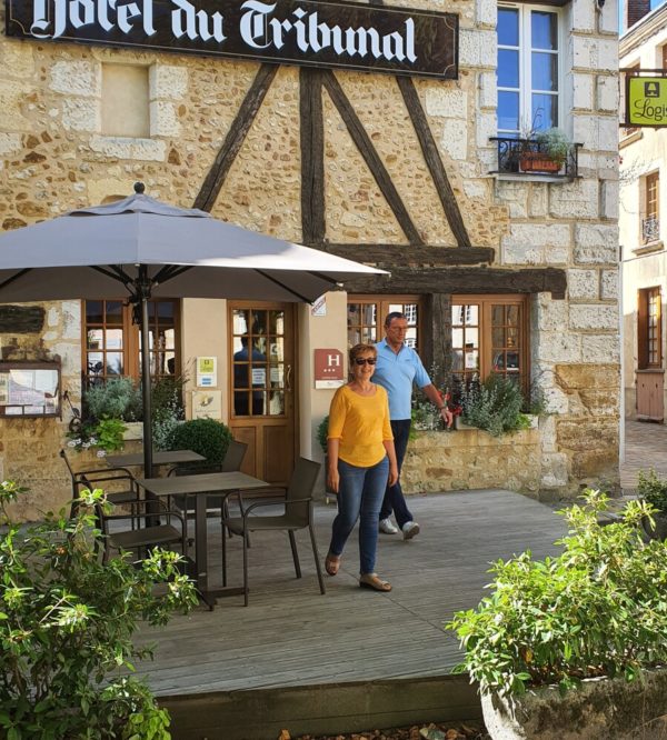 Terrasse de l'hôtel du Tribunal. Deux personne en sorte. Le parasol est déployé, le soleil est présent.