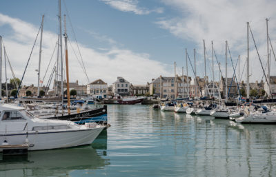 Port de Saint-Vaast-la-Hougue en Normandie, avec bateaux de pêche amarrés et maisons du littoral en arrière-plan.