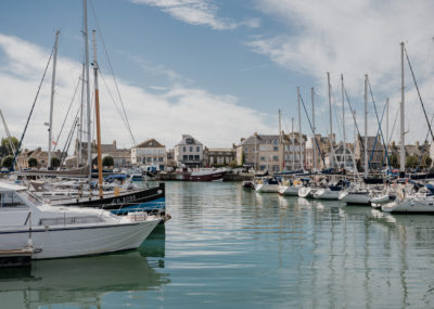 Port de Saint-Vaast-la-Hougue en Normandie, avec bateaux de pêche amarrés et maisons du littoral en arrière-plan.