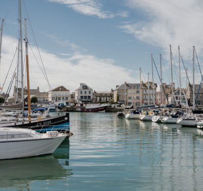 Port de Saint-Vaast-la-Hougue en Normandie, avec bateaux de pêche amarrés et maisons du littoral en arrière-plan.
