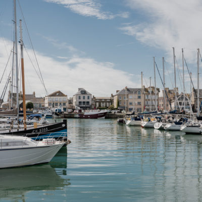 Port de Saint-Vaast-la-Hougue en Normandie, avec bateaux de pêche amarrés et maisons du littoral en arrière-plan.