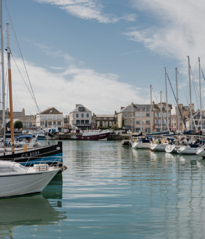 Port de Saint-Vaast-la-Hougue en Normandie, avec bateaux de pêche amarrés et maisons du littoral en arrière-plan.