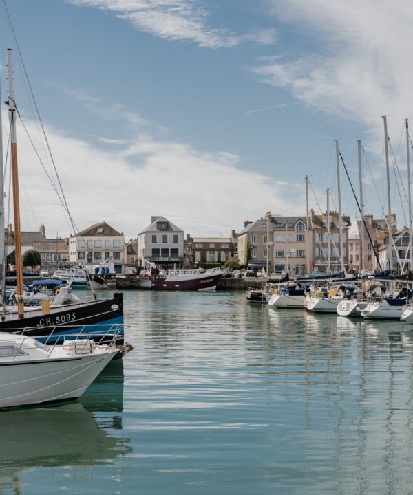 Port de Saint-Vaast-la-Hougue en Normandie, avec bateaux de pêche amarrés et maisons du littoral en arrière-plan.