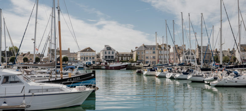 Port de Saint-Vaast-la-Hougue en Normandie, avec bateaux de pêche amarrés et maisons du littoral en arrière-plan.