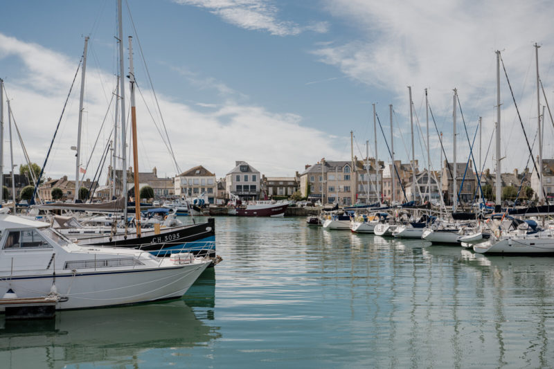 Port de Saint-Vaast-la-Hougue en Normandie, avec bateaux de pêche amarrés et maisons du littoral en arrière-plan.