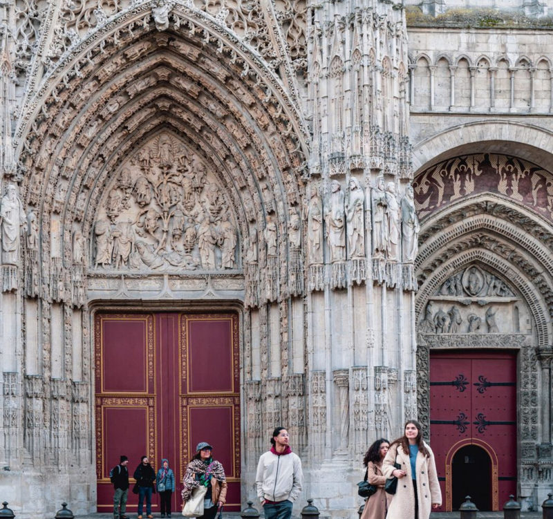 Parvis de la cathédrale de Rouen, plusieurs personnes occupe l'espace devant, mettant en avant la grandeur de la cathédrale.
