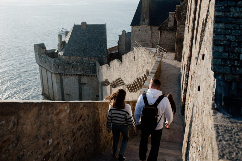 Remparts du Mont-Saint-Michel, une femme et un homme descendent les escaliers. La prise de vue de haut permet d'observer les remparts et la baie.