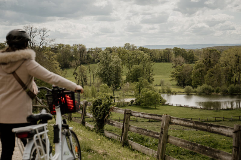 Personne à côté de son vélo face à une prairie et un petit étang