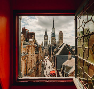 Vue sur la cathédrale de Rouen depuis une fenêtre du Gros Horloge. Les murs autour de la fenêtre sont rouges. La vitre, ouverte, est de style ancien.