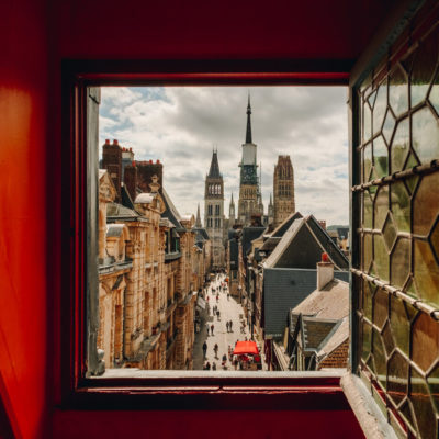 Vue sur la cathédrale de Rouen depuis une fenêtre du Gros Horloge. Les murs autour de la fenêtre sont rouges. La vitre, ouverte, est de style ancien.