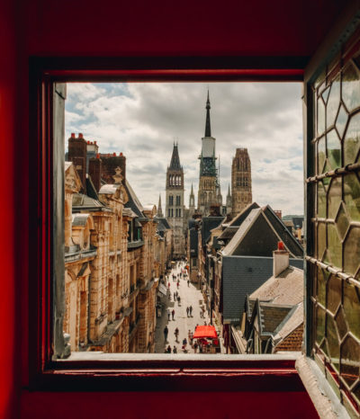 Vue sur la cathédrale de Rouen depuis une fenêtre du Gros Horloge. Les murs autour de la fenêtre sont rouges. La vitre, ouverte, est de style ancien.