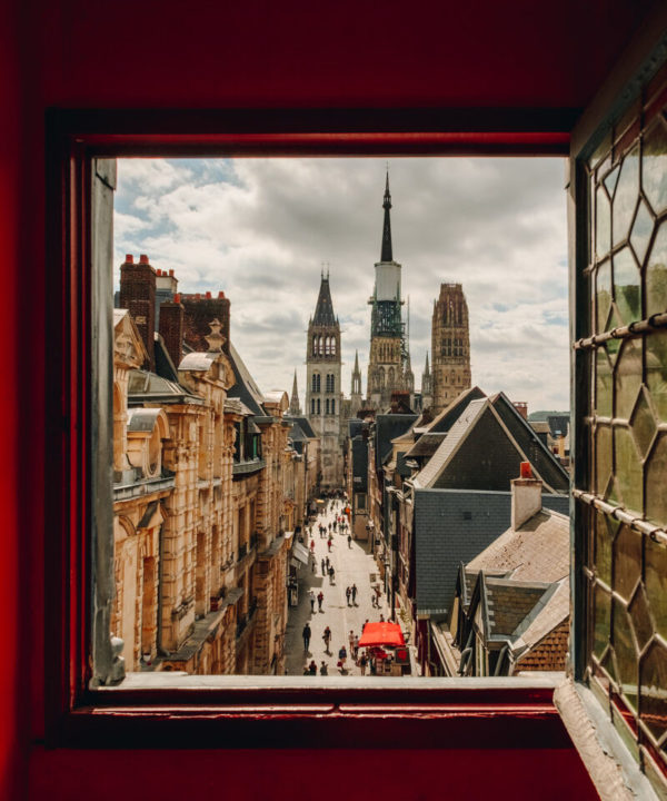 Vue sur la cathédrale de Rouen depuis une fenêtre du Gros Horloge. Les murs autour de la fenêtre sont rouges. La vitre, ouverte, est de style ancien.