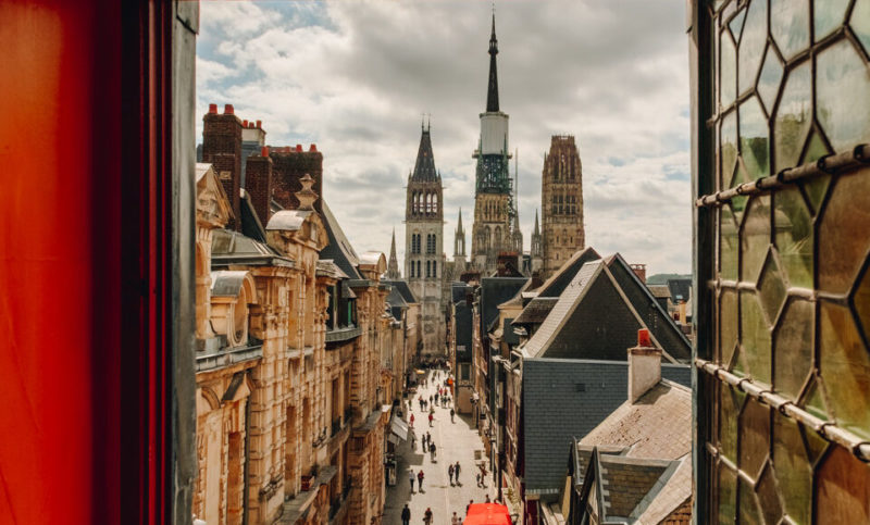 Vue sur la cathédrale de Rouen depuis une fenêtre du Gros Horloge. Les murs autour de la fenêtre sont rouges. La vitre, ouverte, est de style ancien.