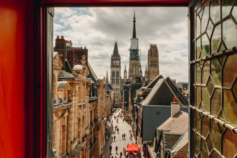 Vue sur la cathédrale de Rouen depuis une fenêtre du Gros Horloge. Les murs autour de la fenêtre sont rouges. La vitre, ouverte, est de style ancien.