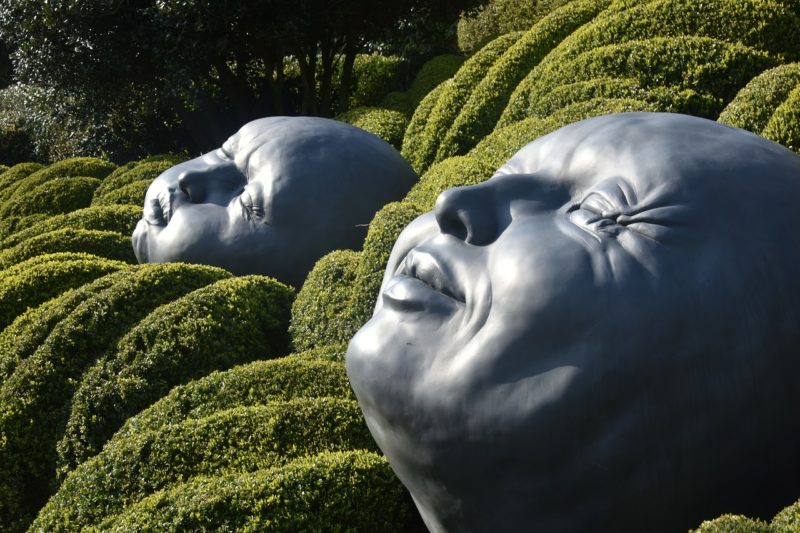Grandes sculptures contemporaines représentant des visages humains sculptés dans la pierre blanche, installées dans les Jardins d’Étretat en Normandie.